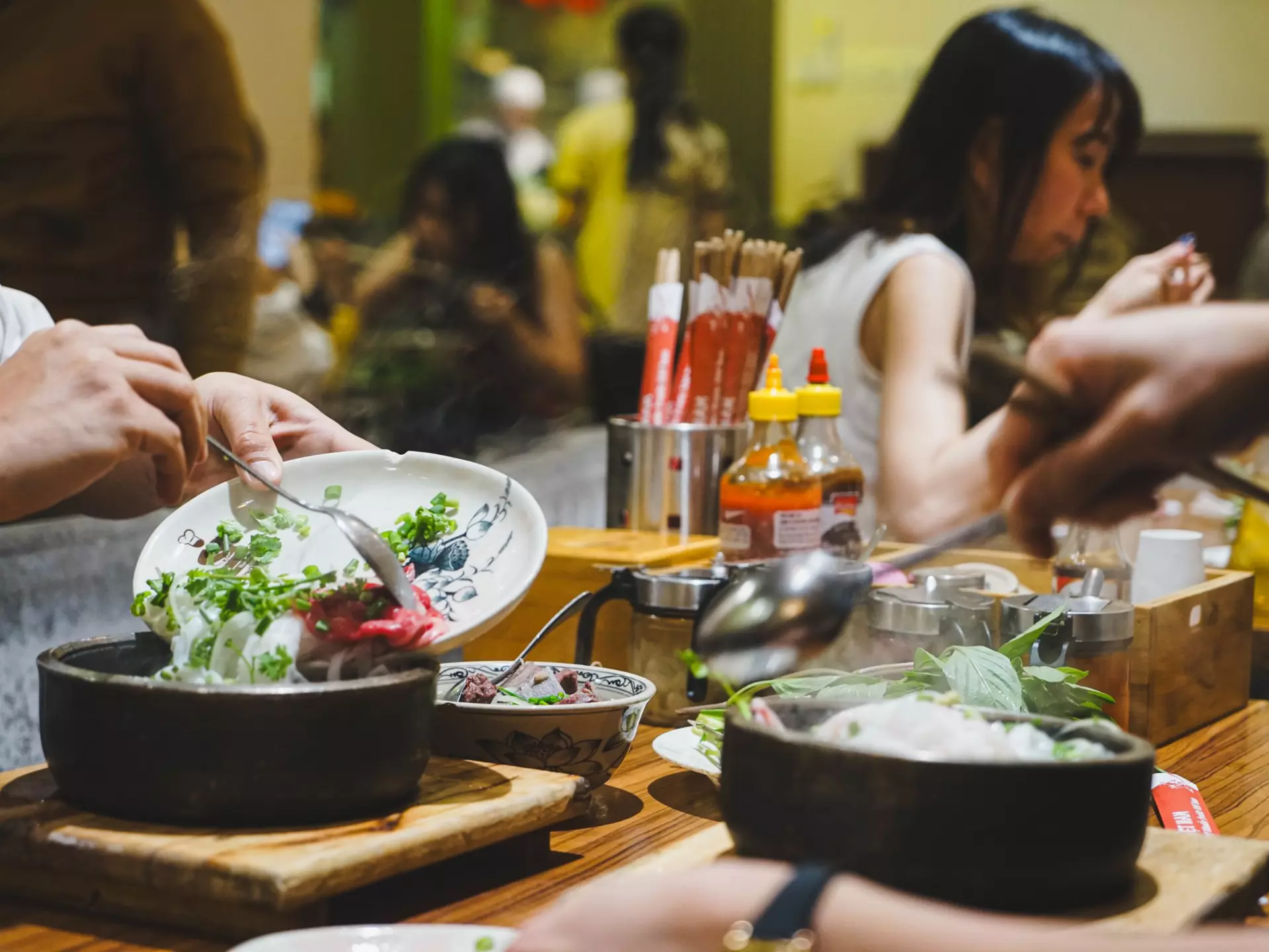People put their forks and spoons into servings of pho at the table of a restaurant.