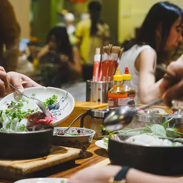 People put their forks and spoons into servings of pho at the table of a restaurant.