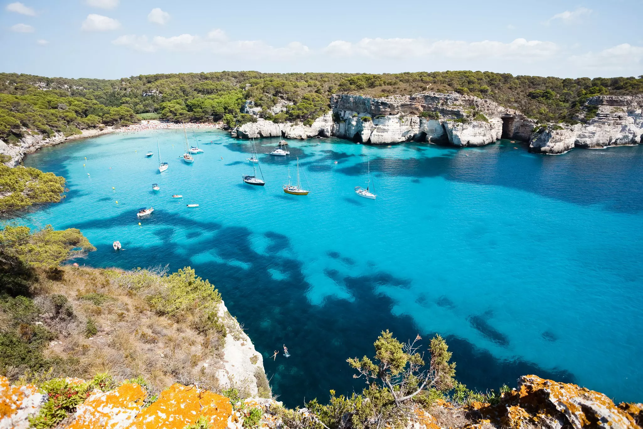 Boats sit in a deep blue coastline in Spain.