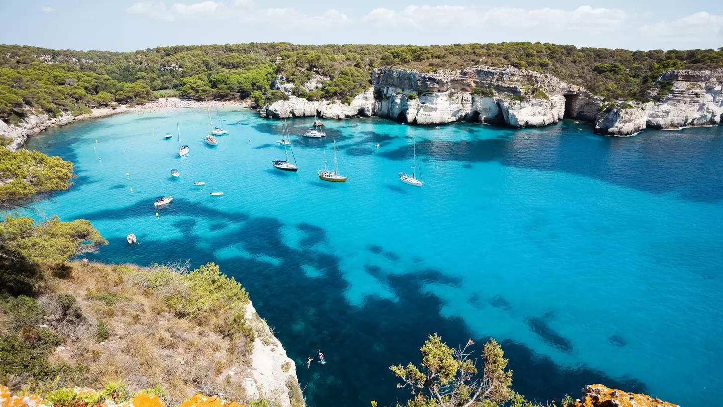 Cala Macarella, with boats floating in the clear waters.