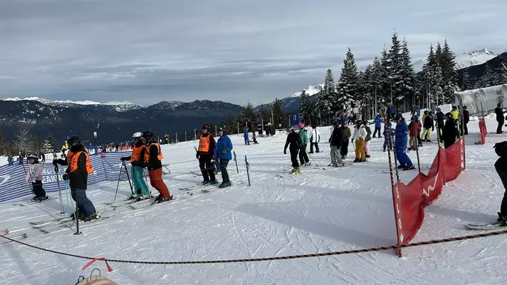 Several groups of skiers wait for a ski lift at a snow-covered slope