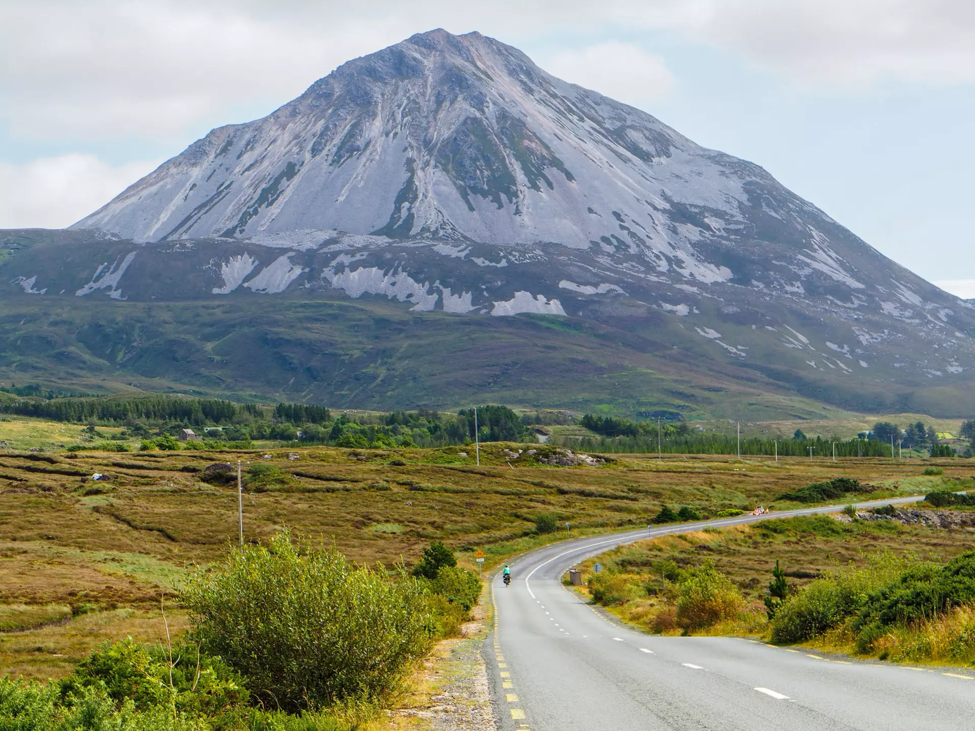 Wild Atlantic Way - Cyclist riding on a road with the Mount Errigal in the background. Co. Donegal, Ireland. August 2022