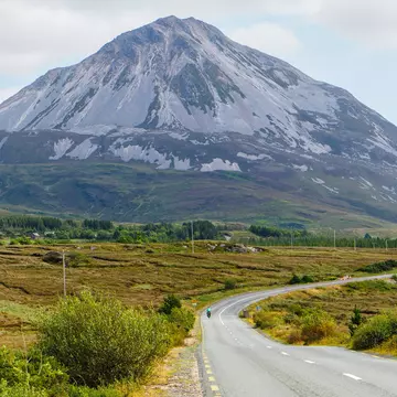 Wild Atlantic Way - Cyclist riding on a road with the Mount Errigal in the background. Co. Donegal, Ireland. August 2022