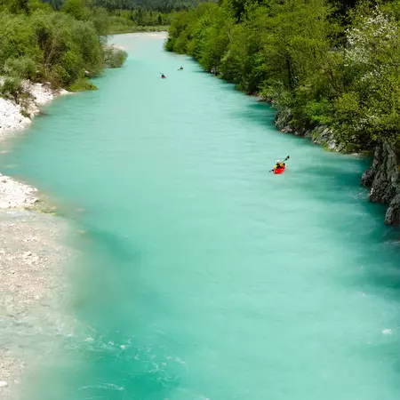 Kayaks on a turquoise river lined by woodland.