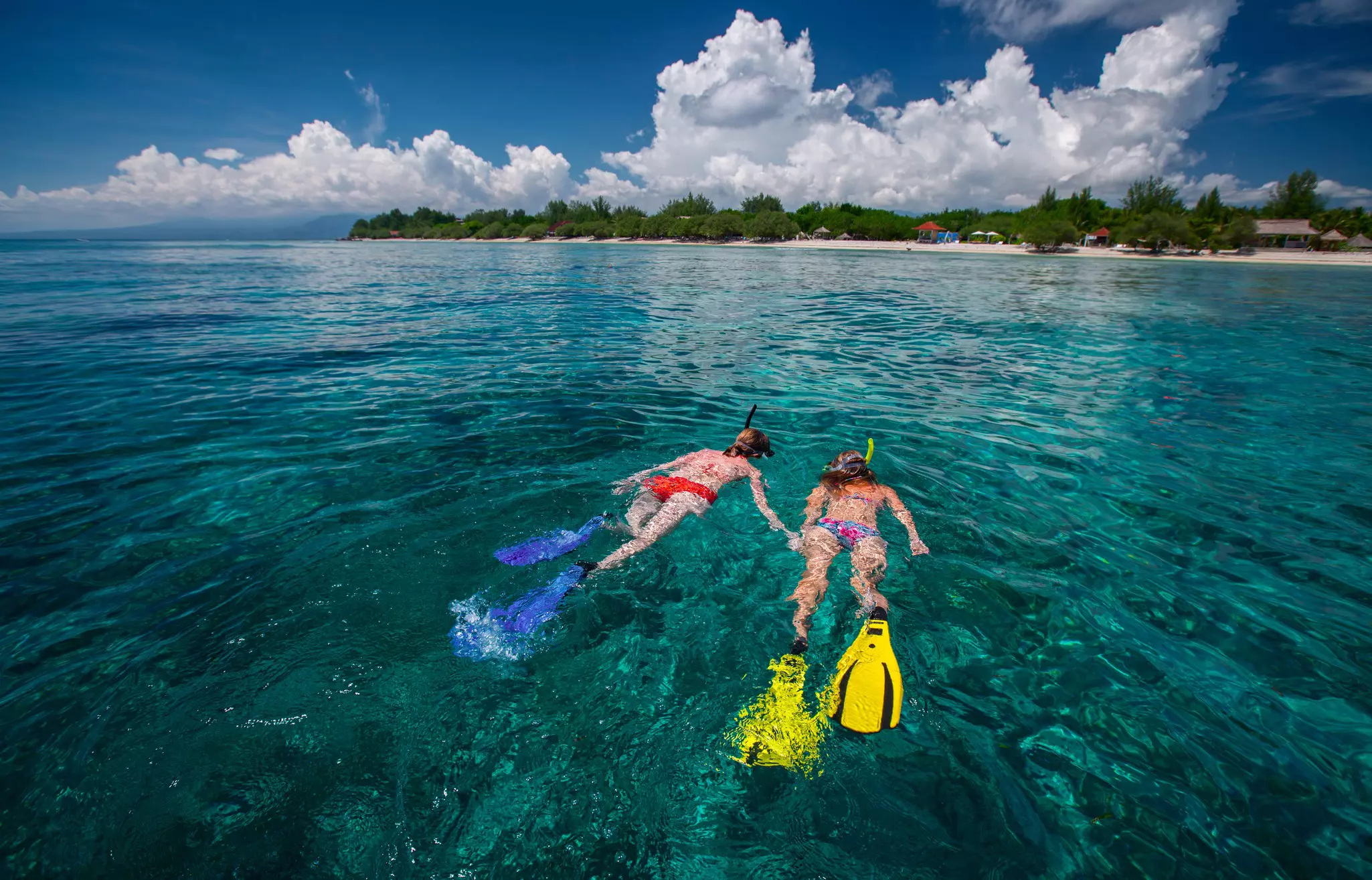 Two ladies snorkeling in tropical clear sea near the green island at sunny day. Gili Trawangan island, Indonesia. 