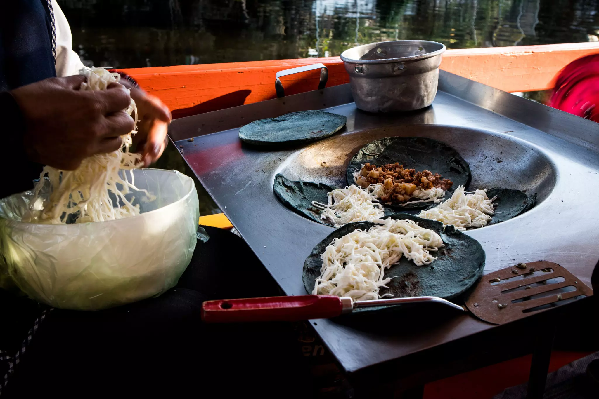 Close-up of blue tortillas being cooked and filled with cheese and meat on a rectangular metal pan with a round insert.