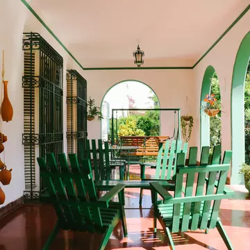 Chairs and a table on a veranda with arches in a city in the tropics.