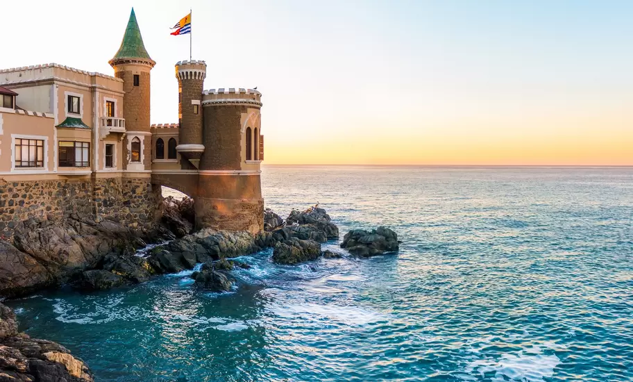 Castillo Wulff in Viña del Mar, a turreted stone castle on rocks over the Pacific, with a flag flying at sunset