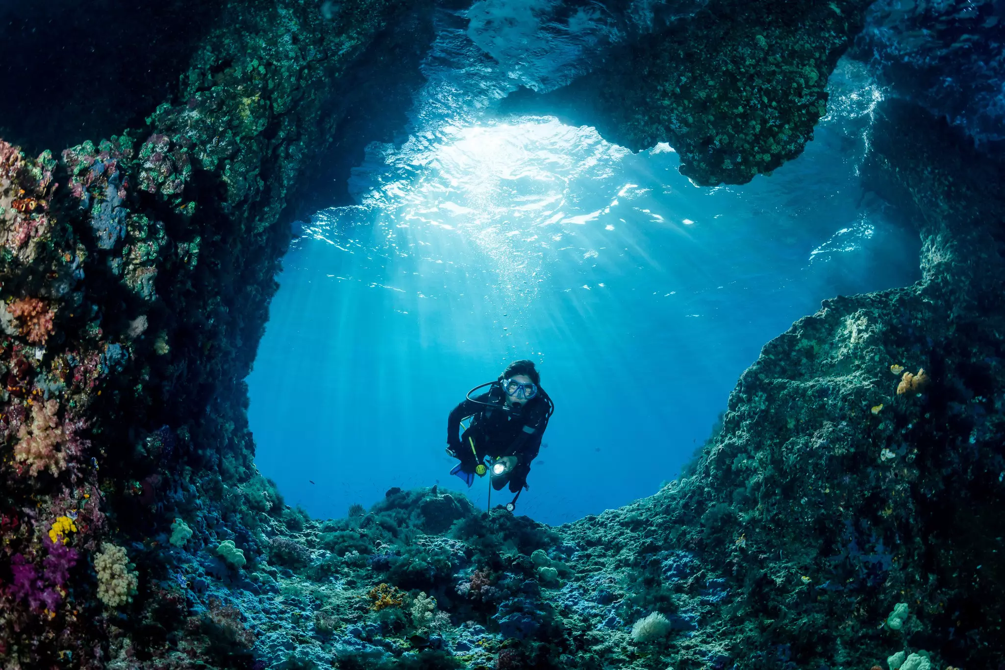 woman diver underwater at the entrance of a cave with sunrays