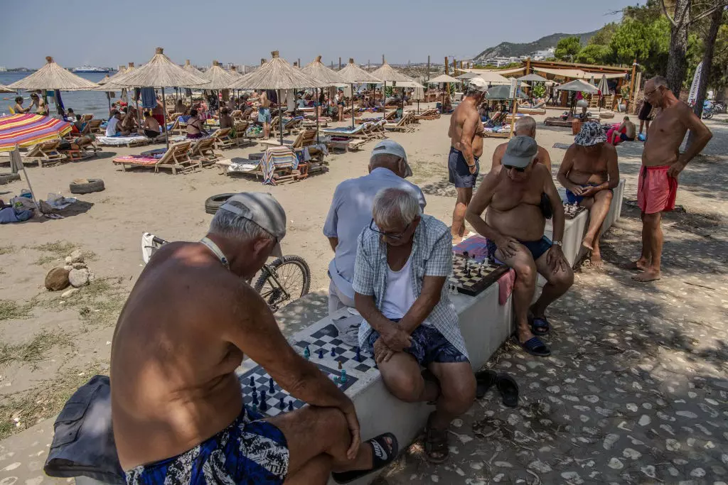 People playing chess by the beach in Vlora, Albania, with sun umbrellas behind.