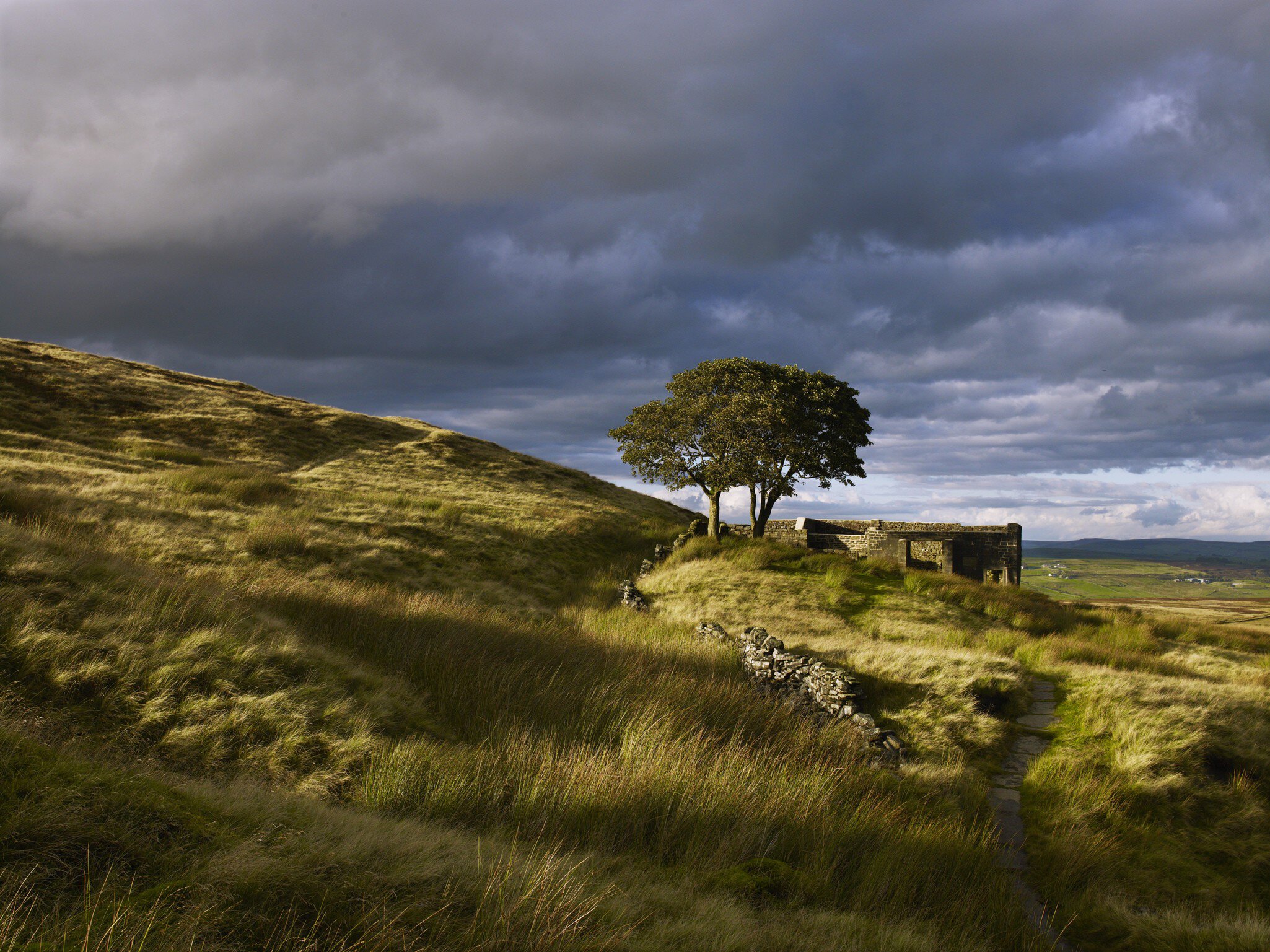Ruins are seen on a grassy moorland under a stormy sky in West Yorkshire, England
