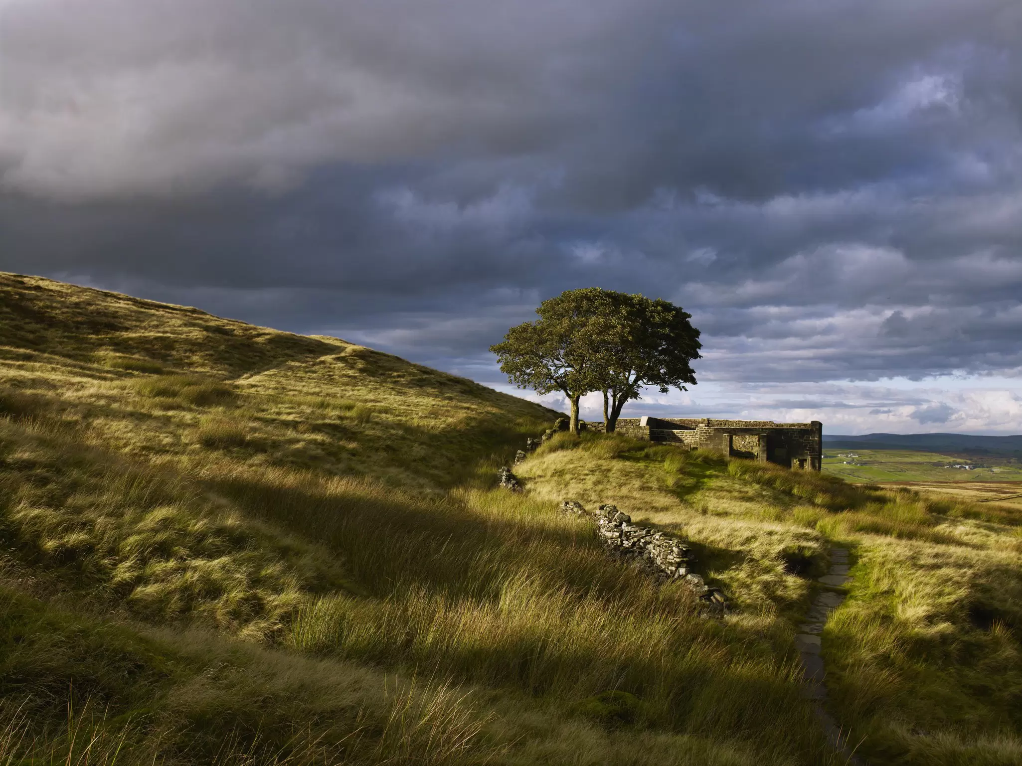 Ruins are seen on a grassy moorland under a stormy sky in West Yorkshire, England