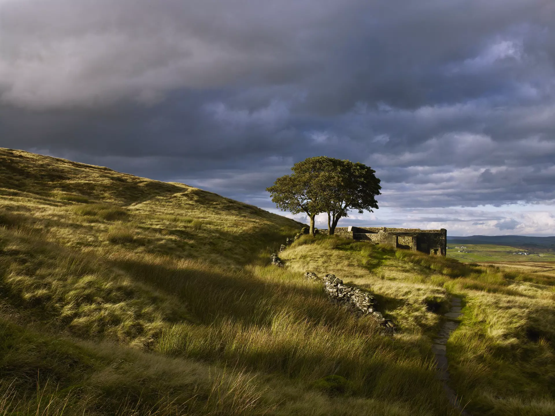 Ruins are seen on a grassy moorland under a stormy sky in West Yorkshire, England