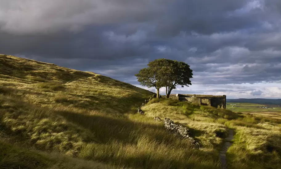 Ruins are seen on a grassy moorland under a stormy sky in West Yorkshire, England