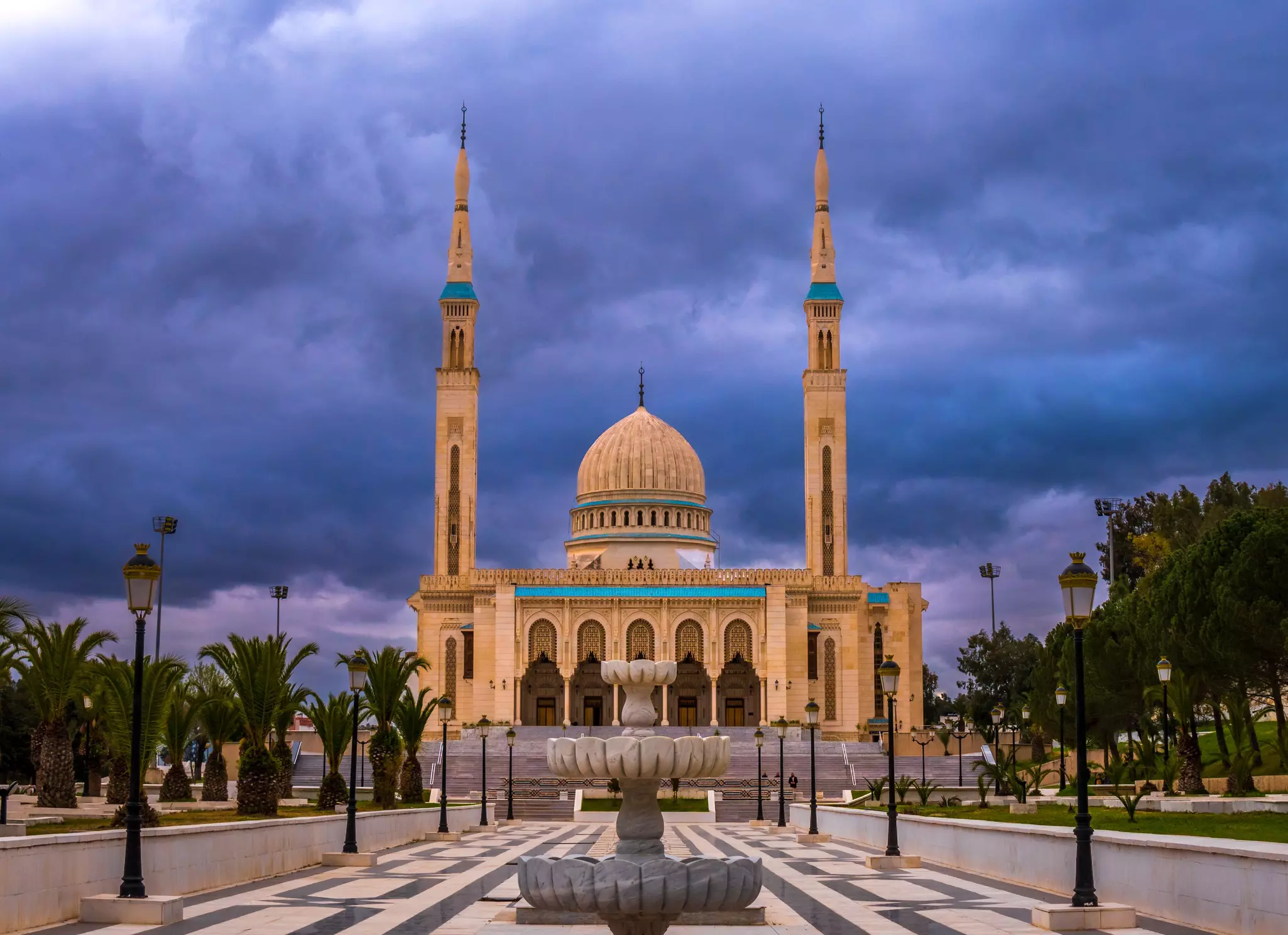 A modern mosque with a central dome and two very tall minarets under a cloudy evening sky.