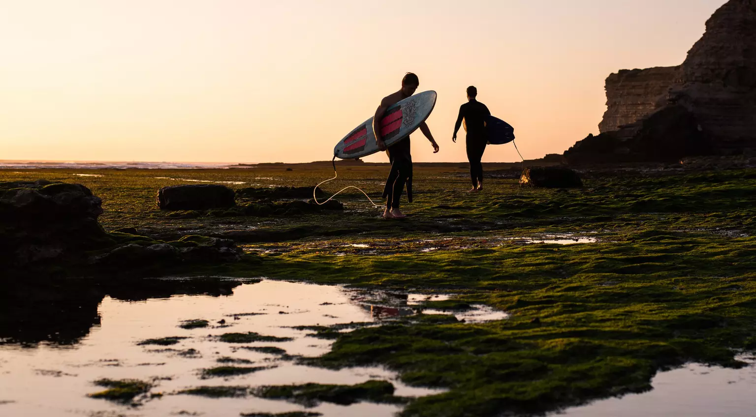 Two surfers carry their boards out to sea during sunset