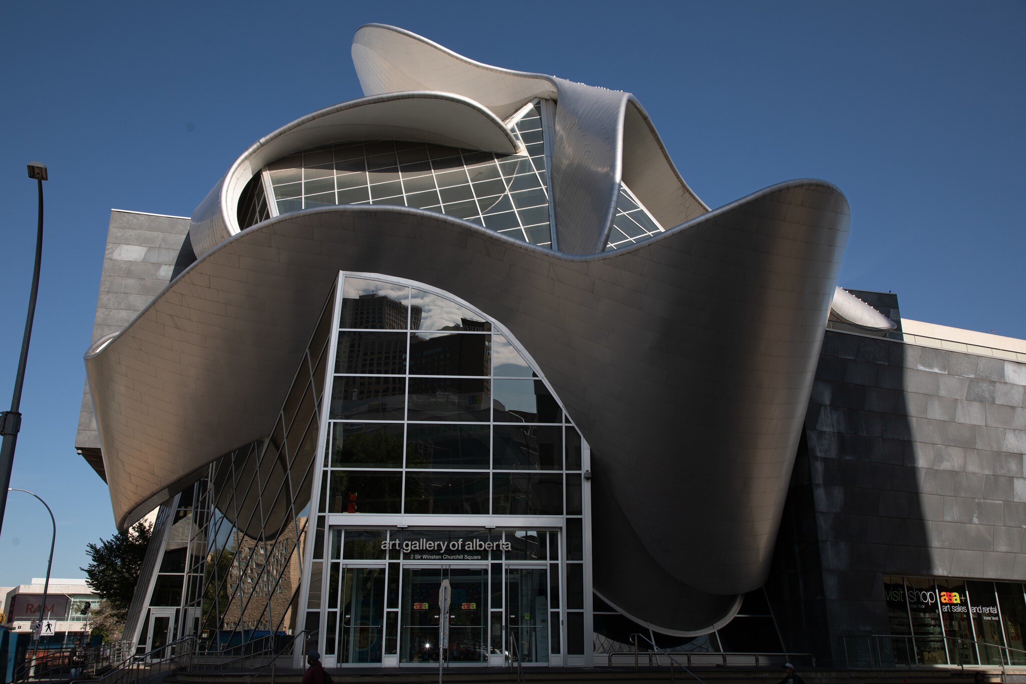 A curving stainless-steel ribbon wrapping a glass-fronted gallery building.