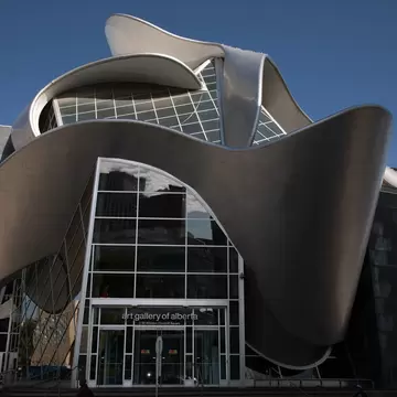 A curving stainless-steel ribbon wrapping a glass-fronted gallery building.