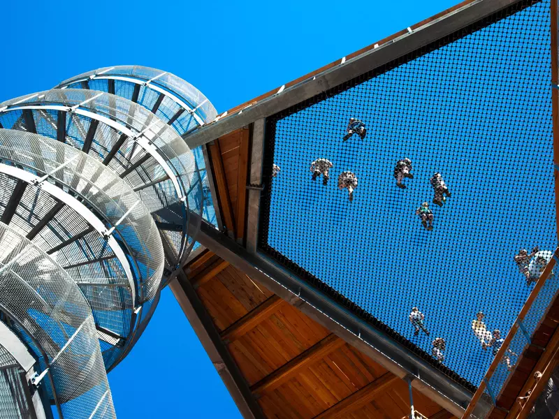 People walk on a mesh platform attached to a column.