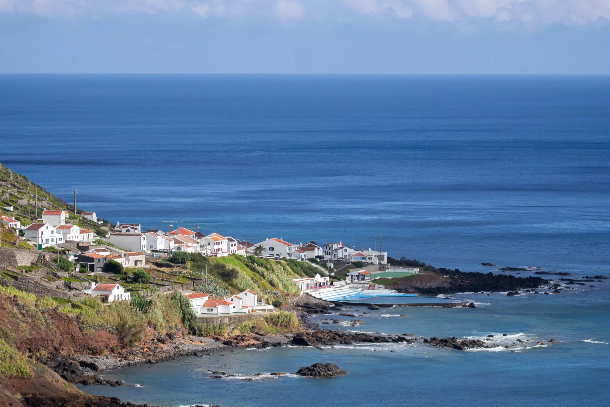 Aerial view of village along a coastline with hills to the left and the ocean beyond.