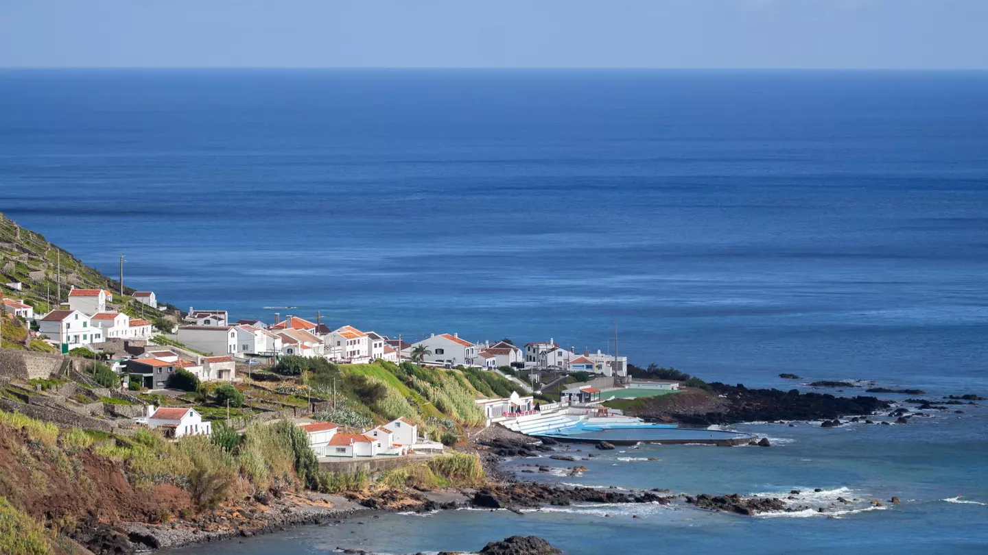 Aerial view of village along a coastline with hills to the left and the ocean beyond.