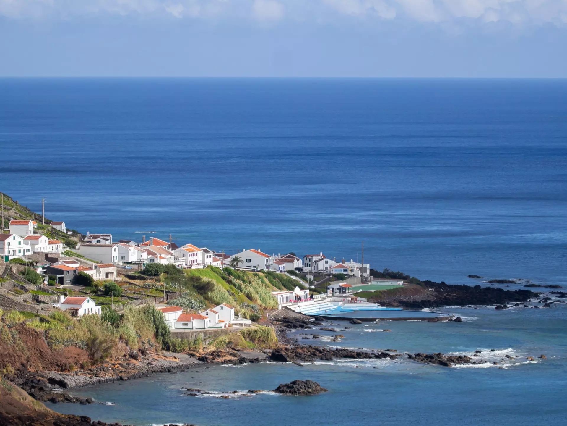 Aerial view of village along a coastline with hills to the left and the ocean beyond.