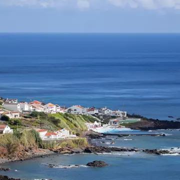 Aerial view of village along a coastline with hills to the left and the ocean beyond.