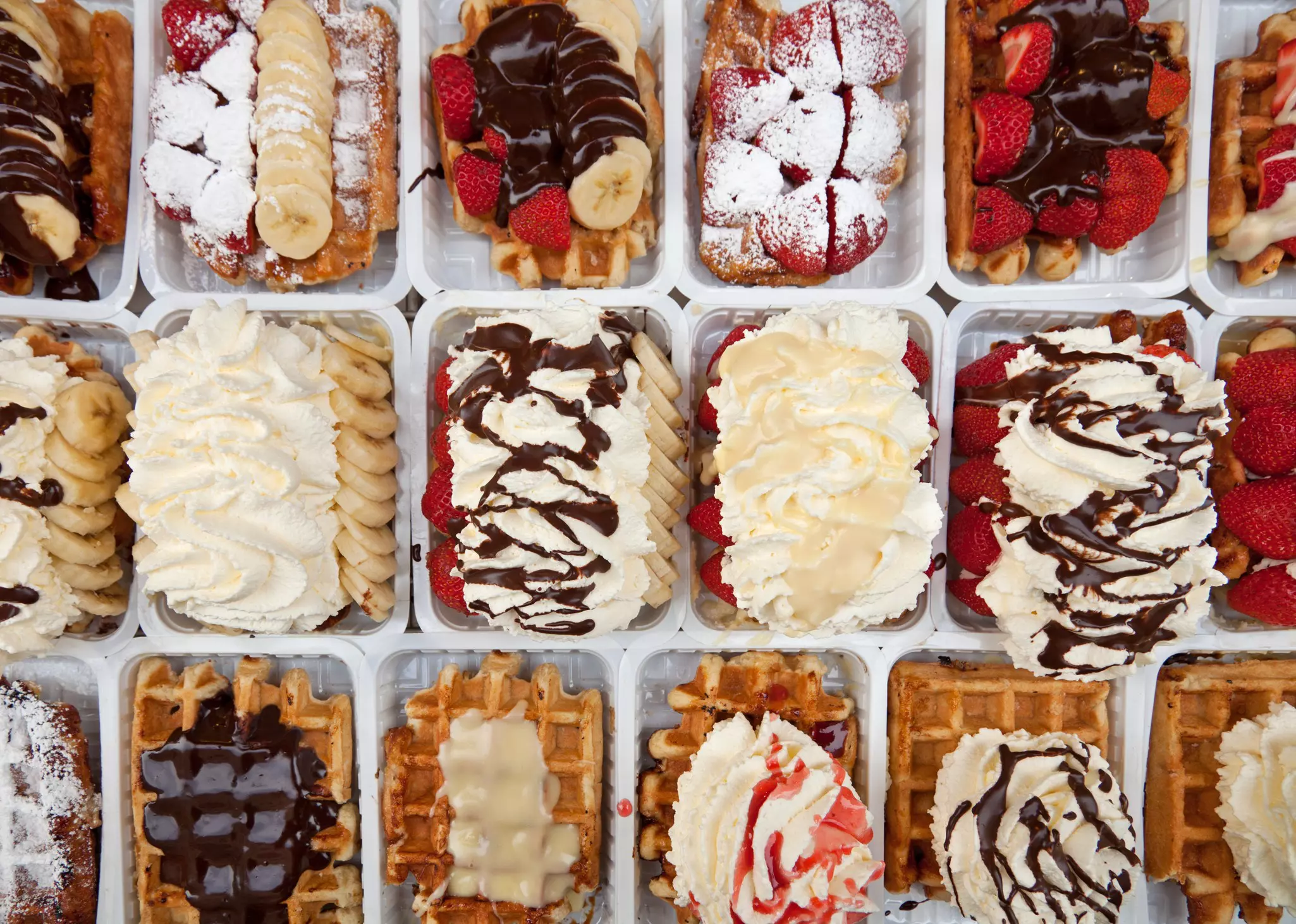 Dozens of waffles topped with syrups, whipped cream and other toppings are on display and photographed from above.