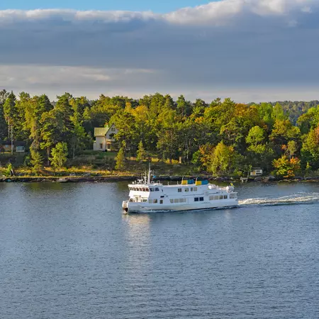 A ferry traveling along beside a forest-covered island in the Stockholm archipelago, Sweden.