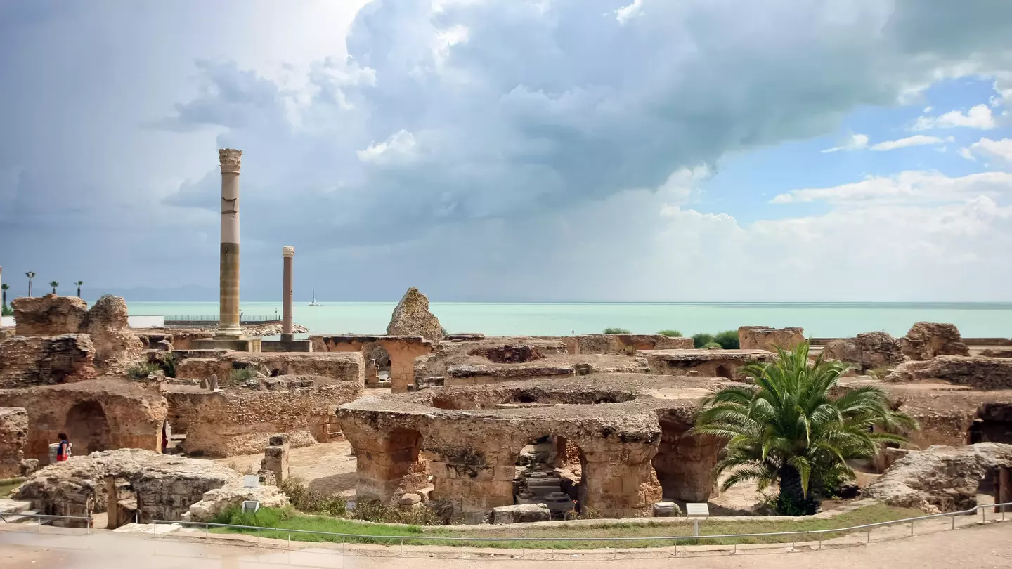 The image looks across a series of thick stone arches and two stone columns towards the sea, which has a thick thunder cloud over it.