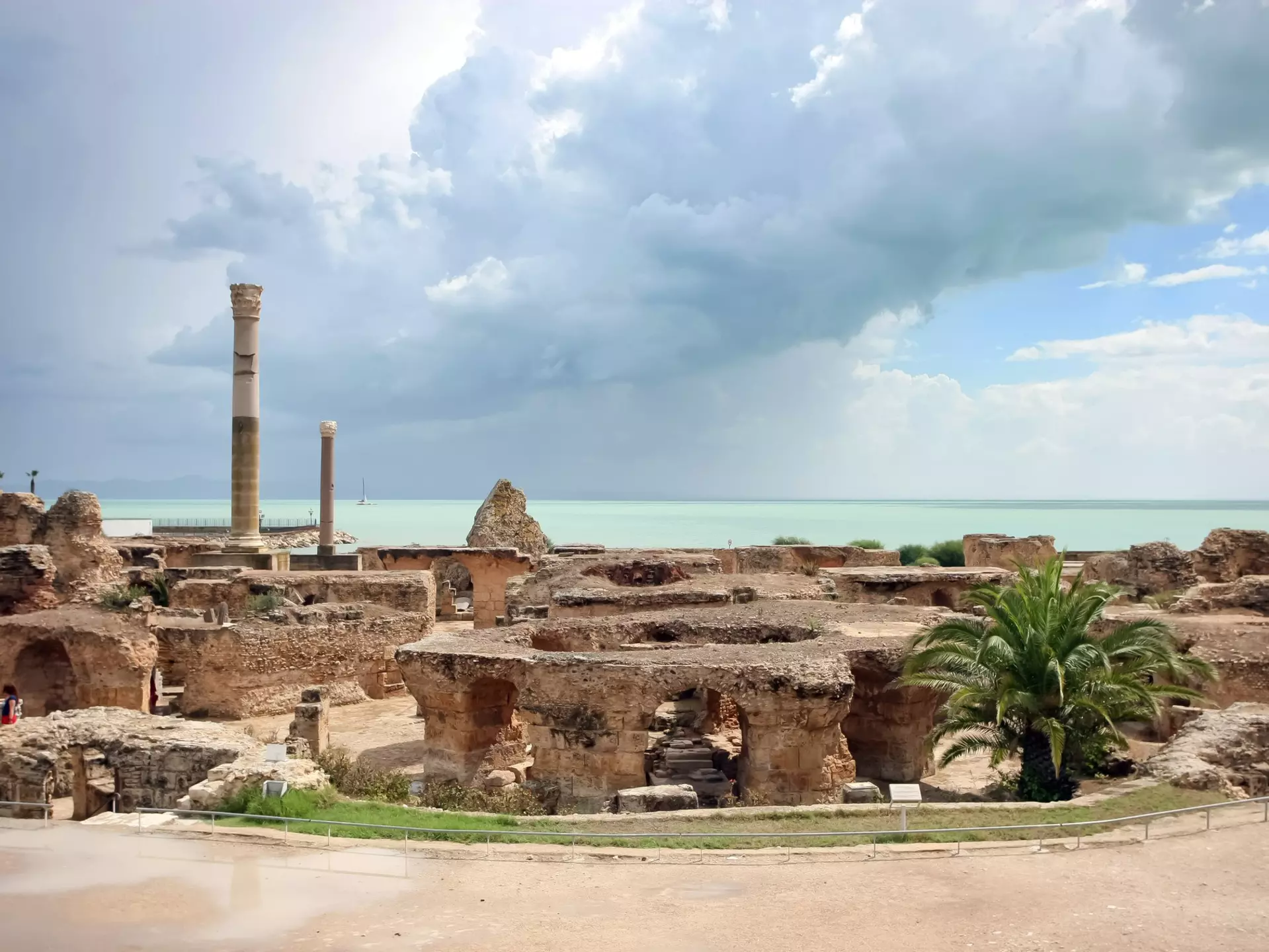 The image looks across a series of thick stone arches and two stone columns towards the sea, which has a thick thunder cloud over it.