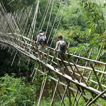 Backpackers crossing bamboo suspension bridge on trek from Kuching to Bidayuh village of Semban, near Kuching.