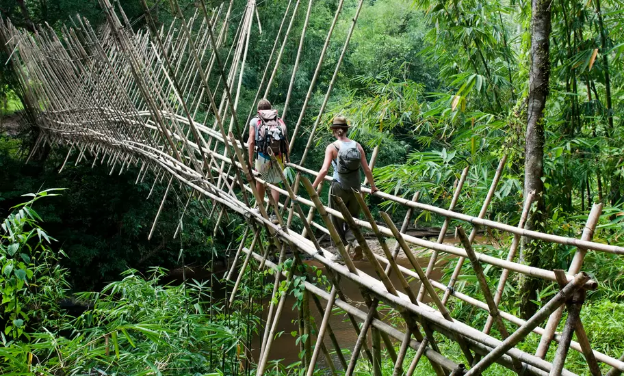 Two hikers crossing a bamboo suspension bridge over a jungle river in Kalimantan, Indonesian Borneo