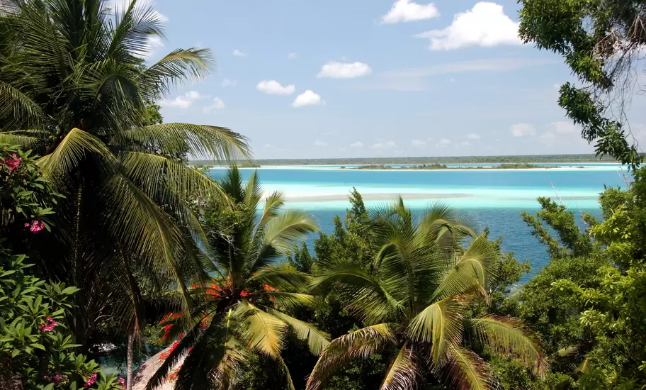 View through palm trees over a vivid turquoise and deep-blue lagoon under scattered clouds