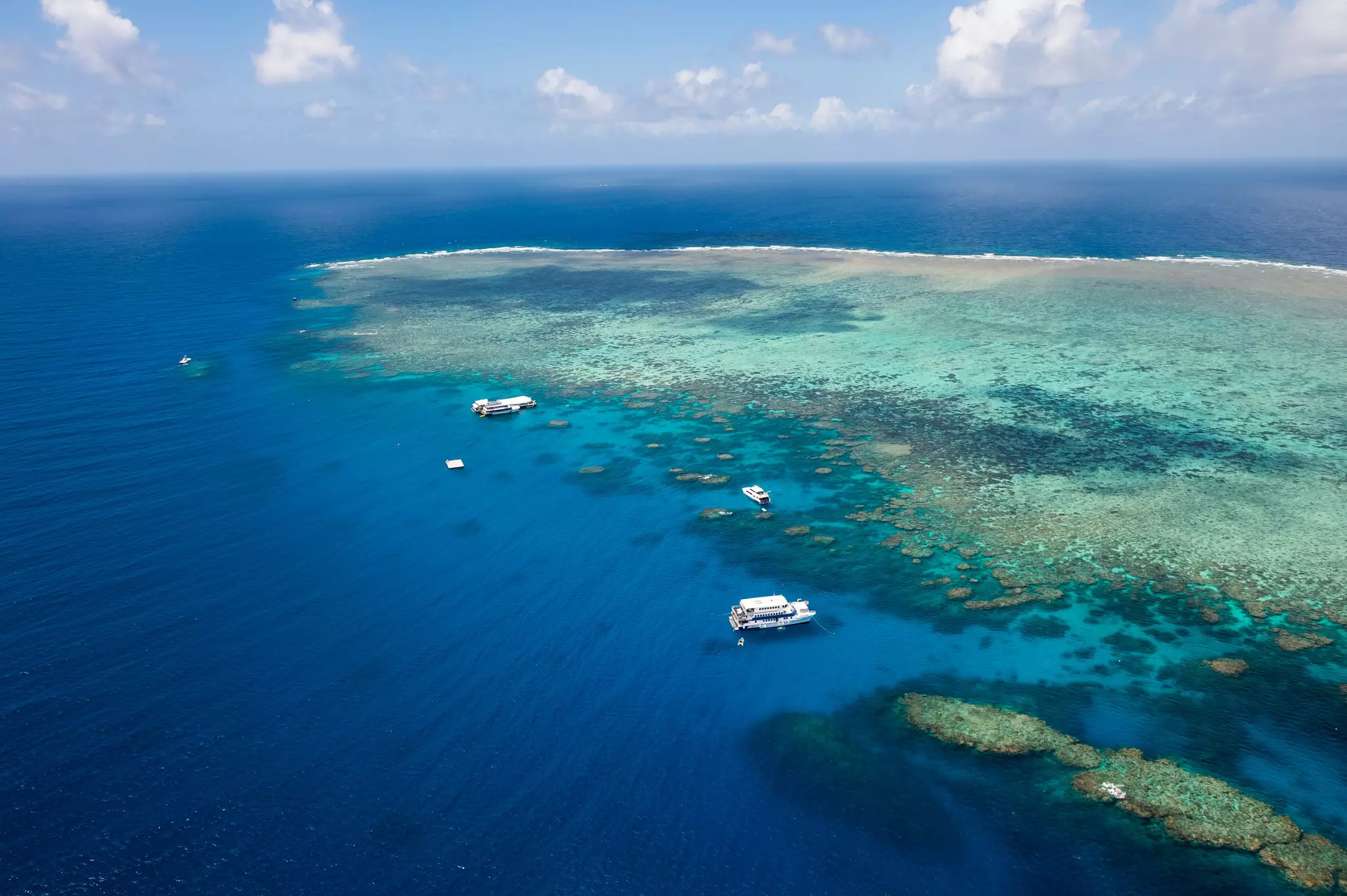 Large floating pontoons docked in the deep blue ocean at the edge of a vast coral reef.