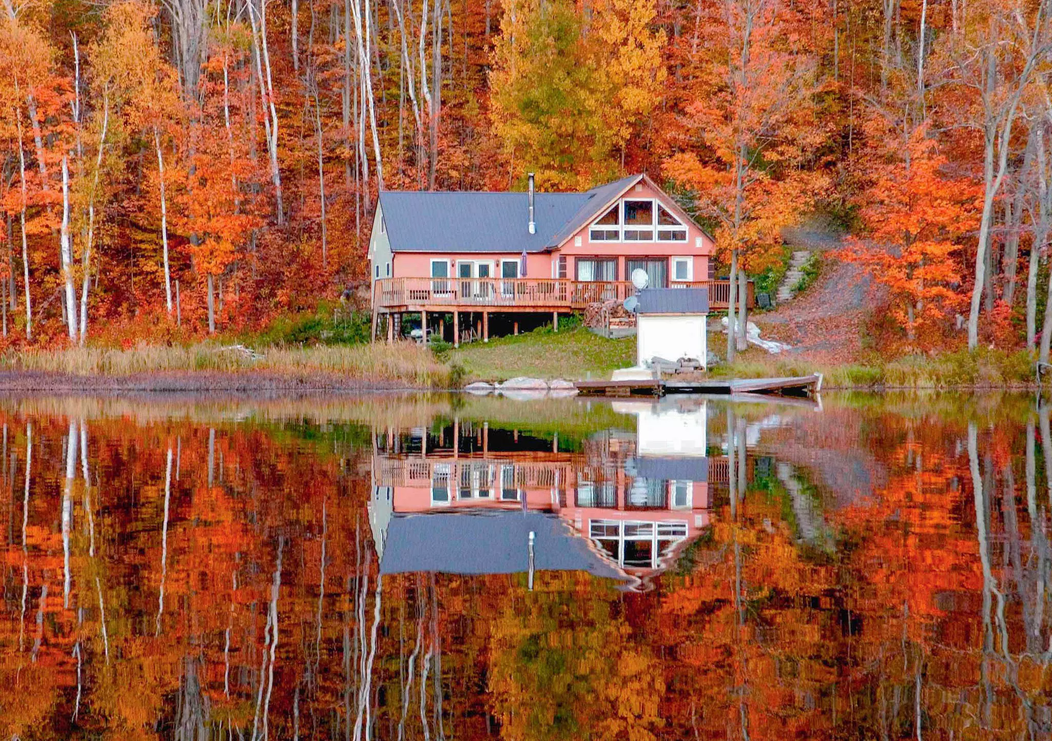 Red cabin surrounded by bright red fall foliage reflecting on a lake in Muskoka, Canada