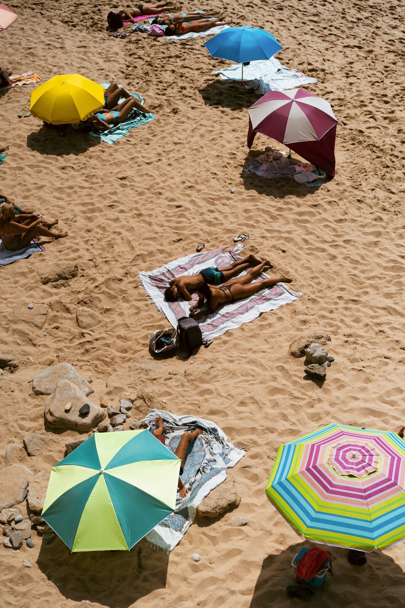 Overhead view of sunbathers on towels and colorful beach umbrellas on golden sand in Cascais, Portugal