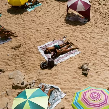 Overhead view of sunbathers on towels and colorful beach umbrellas on golden sand in Cascais, Portugal