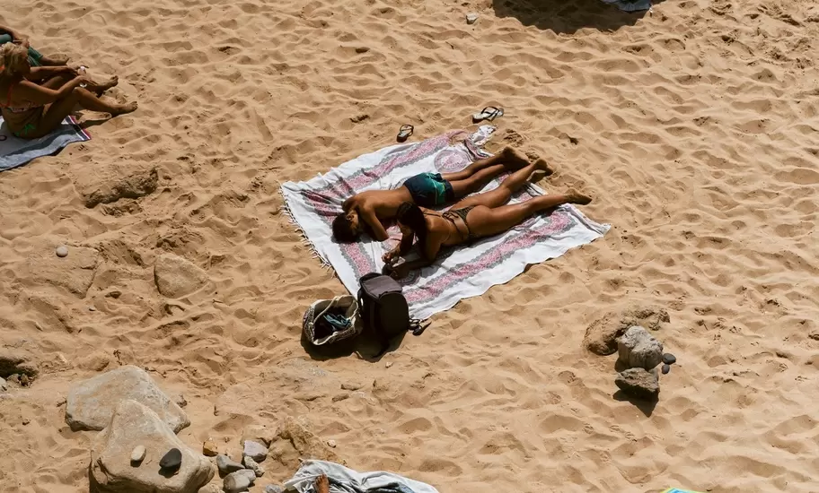 Overhead view of sunbathers on towels and colorful beach umbrellas on golden sand in Cascais, Portugal