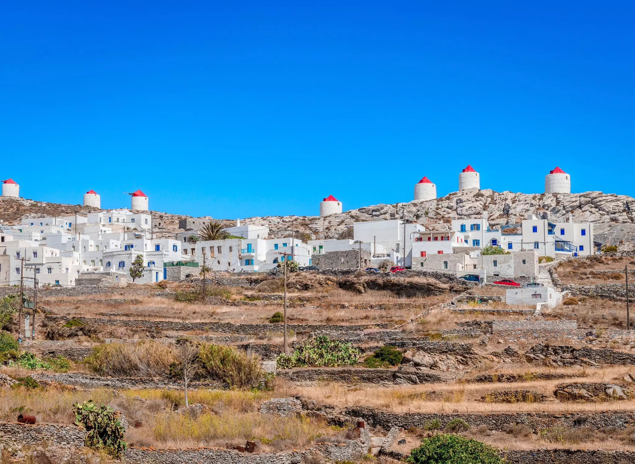 Whitewashed houses and windmills on top of a dry hillside in the Cyclades, Greece.