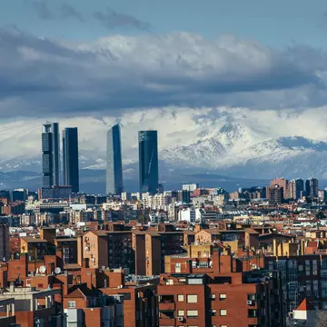 A wide view of a city skyline, including several skyscrapers, with snowy mountains in the distance.