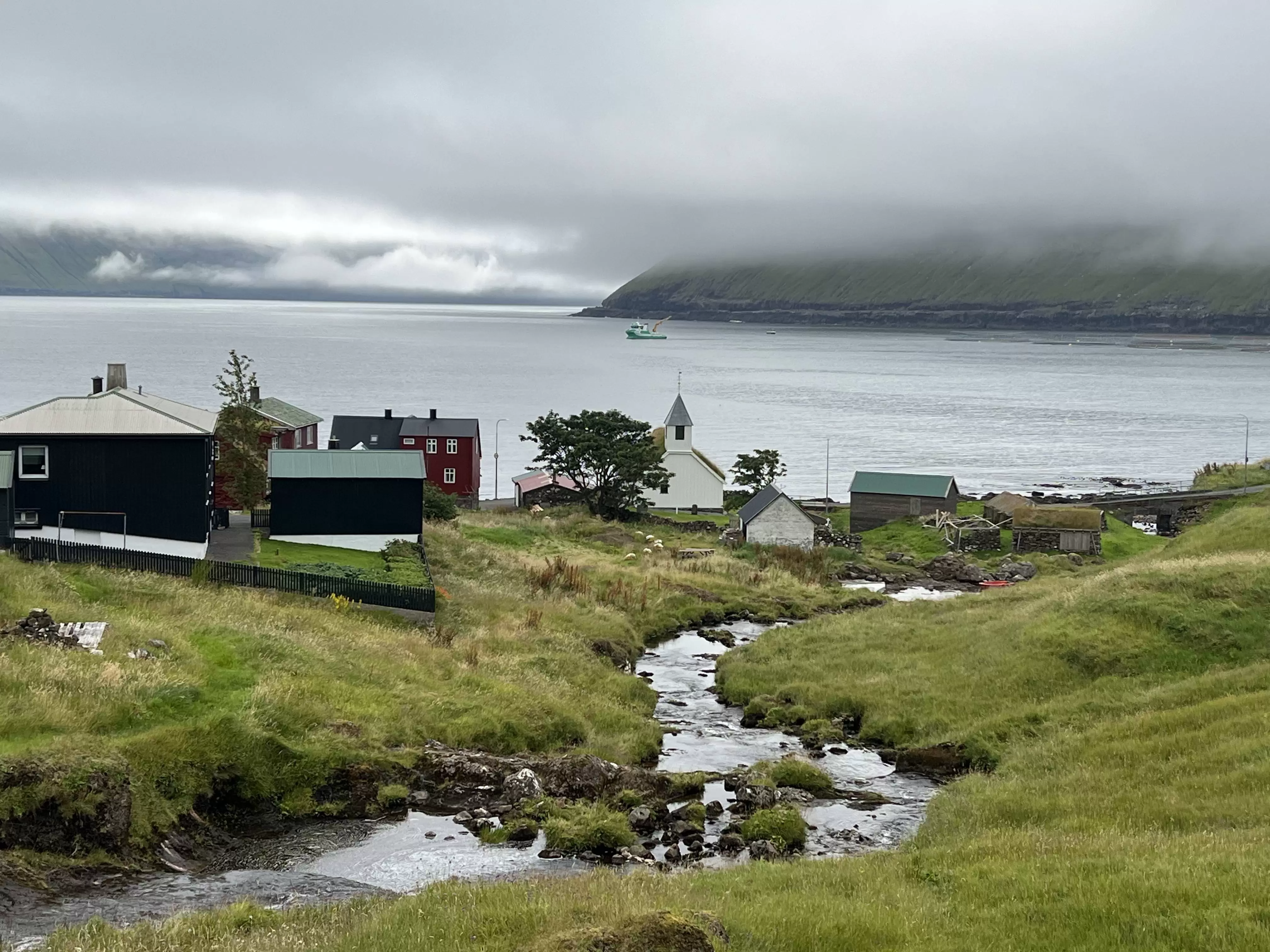 A watery landscape at Oyndarfjørður in the Faroe Islands, with misty clouds over the hills behind the inlet. 