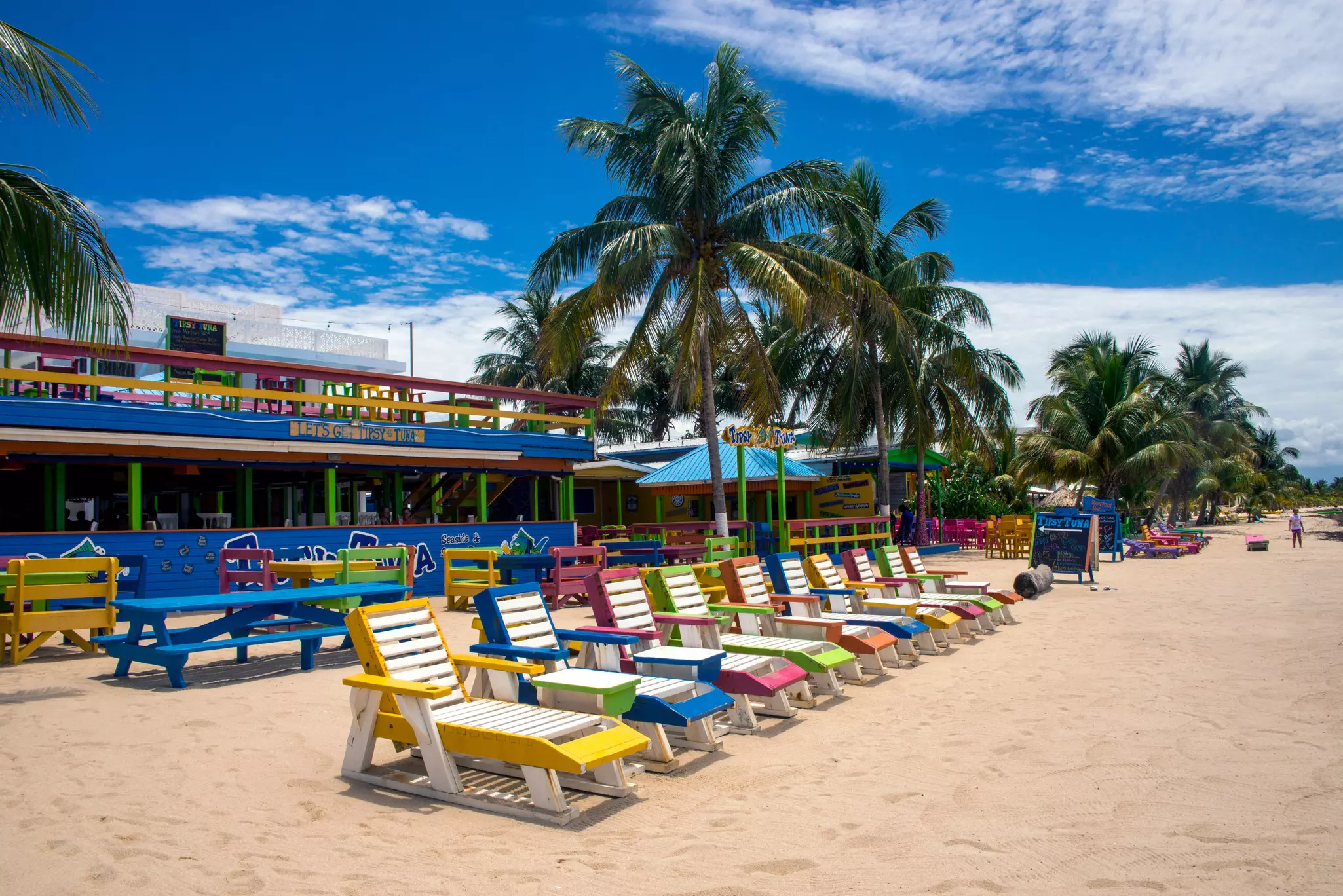 A sandy beach with brightly coloured sunloungers in a row outside a restaurant.