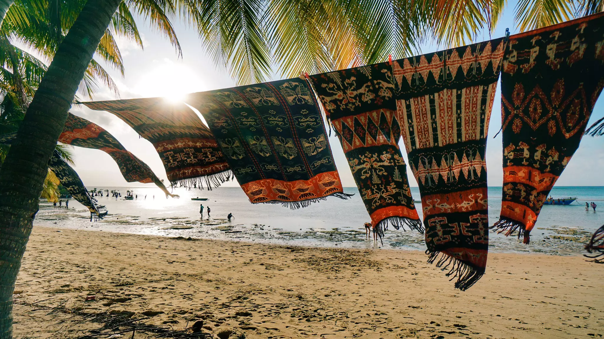 A beach-side washing line filled with woven fabrics fluttering in the breeze on a sunny day.