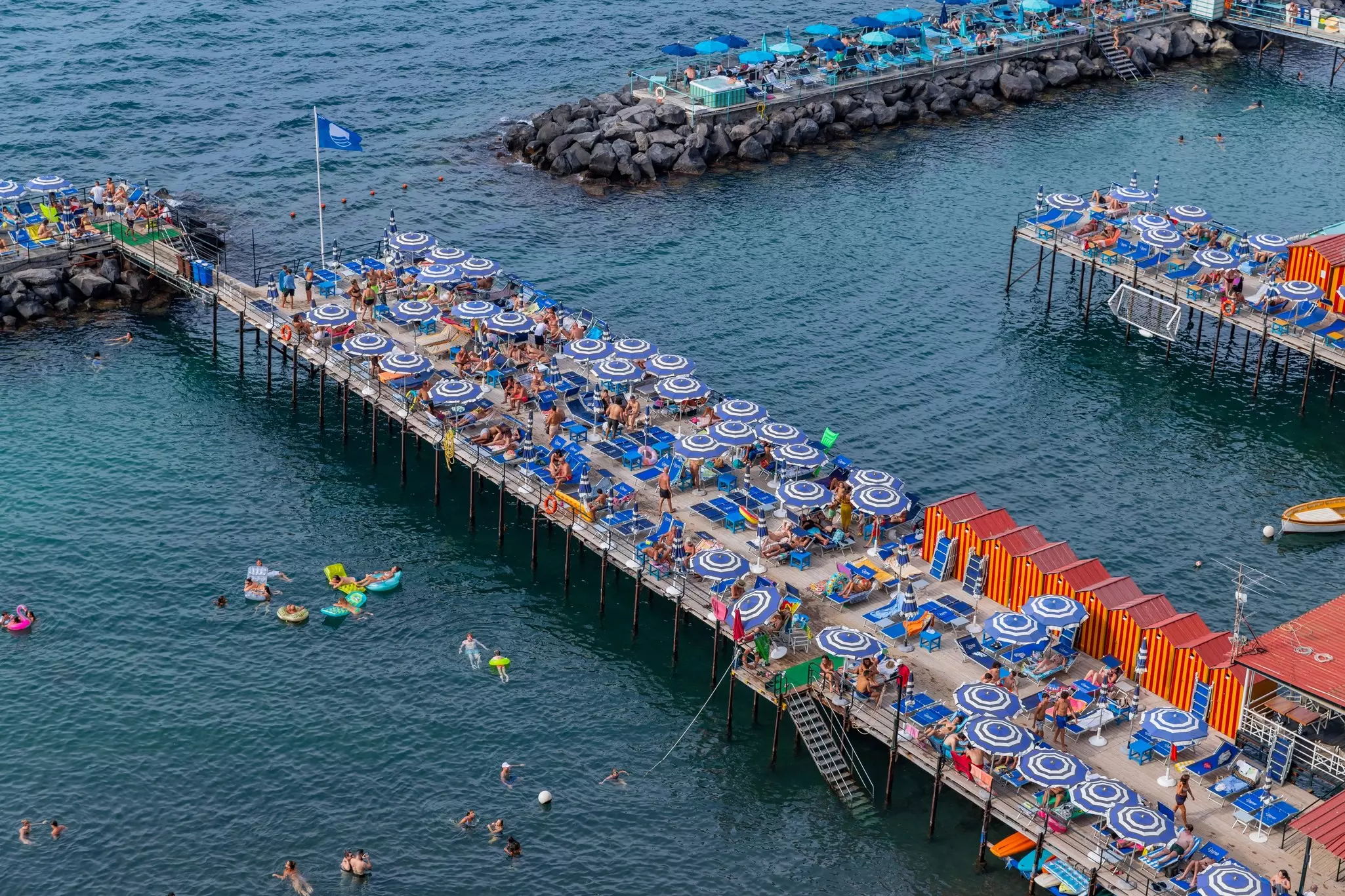A pier lined with blue parasols and people swimming underneath it