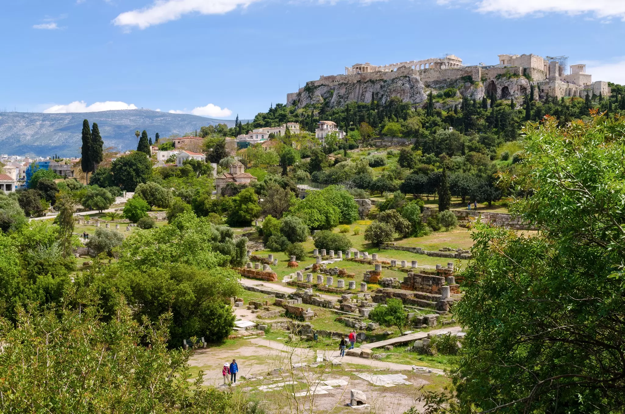 Ancient ruins and blocks of stone fill an archaeological site at the foot of a hill: Athens' ancient Agora (marketplace).