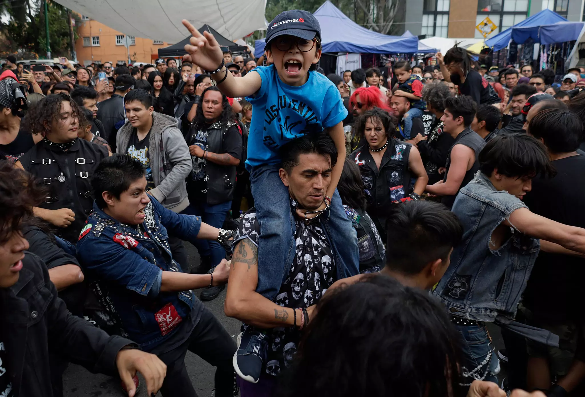 A boy sits on his father’s shoulders in a crowd listening to a heavy-metal concert.