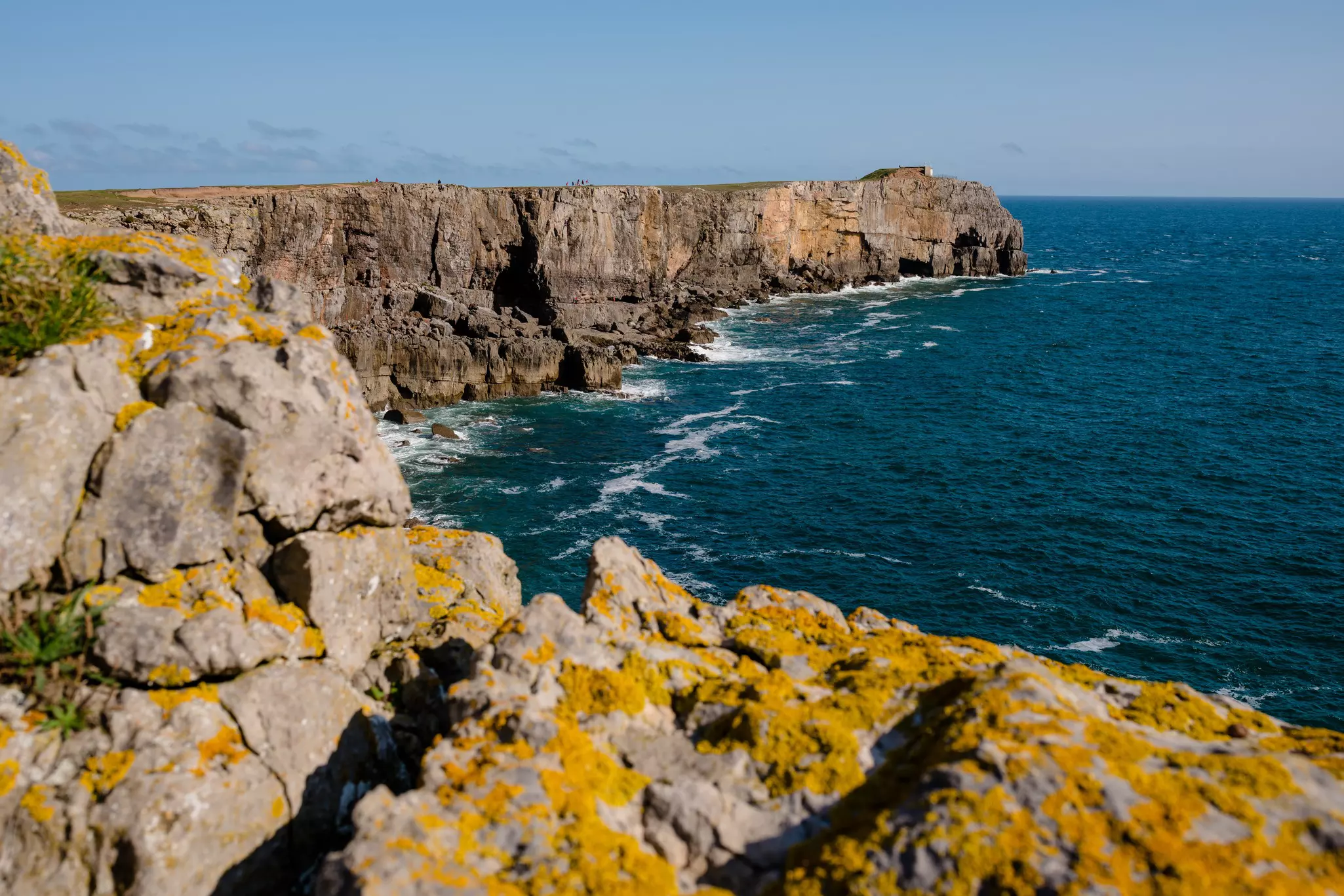 Rocky cliff extending into the sea on a cloudy day, with out-of-focus, lichen-covered rocks in the foreground.
