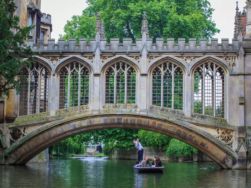 People row boats under the Bridge of Sighs in Cambridge, a covered bridge. 