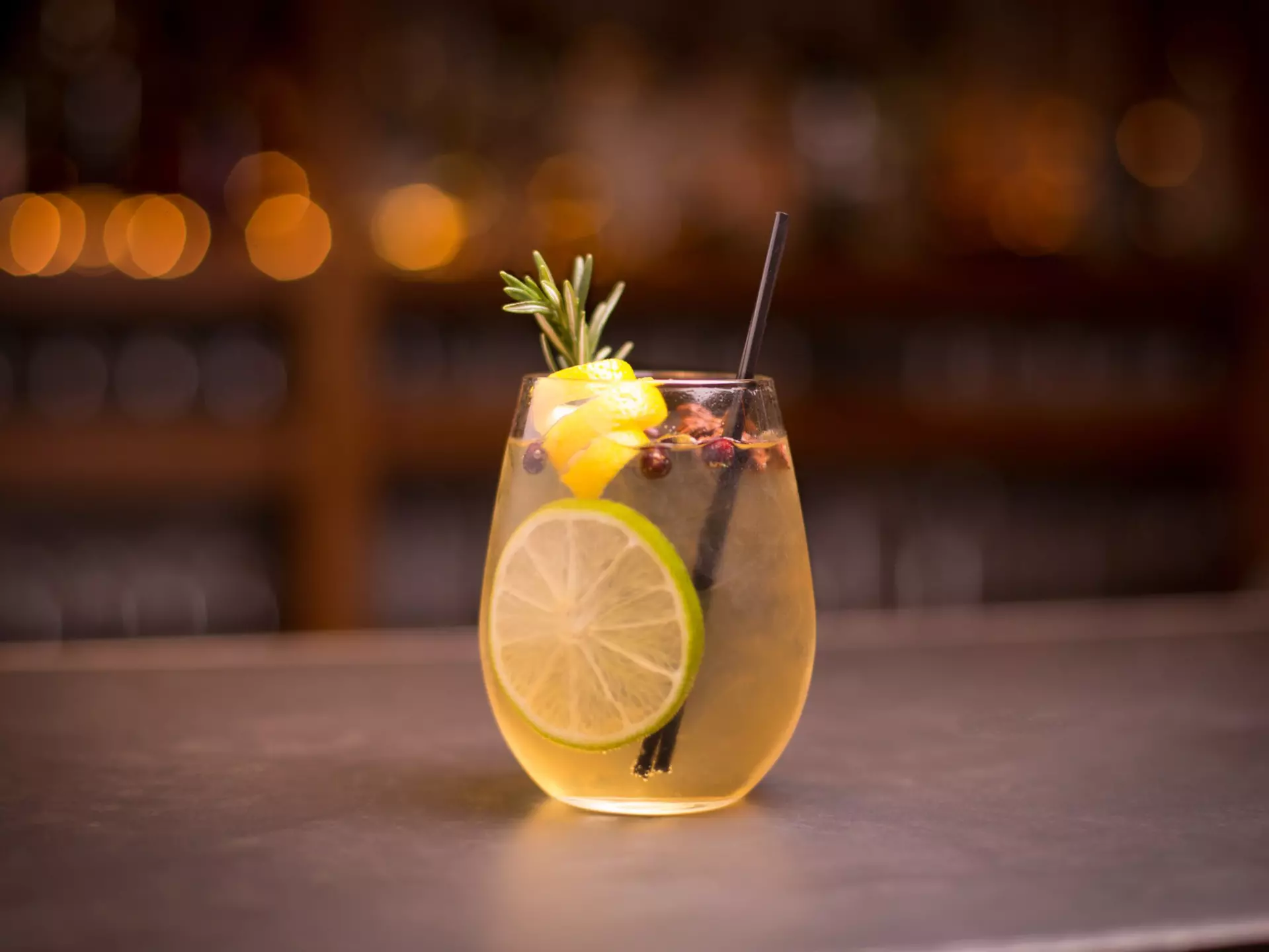 Low angle close up of ice cold modern gourmet craft cocktail of gin and tonic soda garnished by lemon slice and rosemary sprig sprinkled by juniper berries on bar with blurry restaurant bar background  License Type: media  Download Time: 2023-08-29T02:50:24.000Z  User: dermothegarty77  Is Editorial: No  purchase_order: